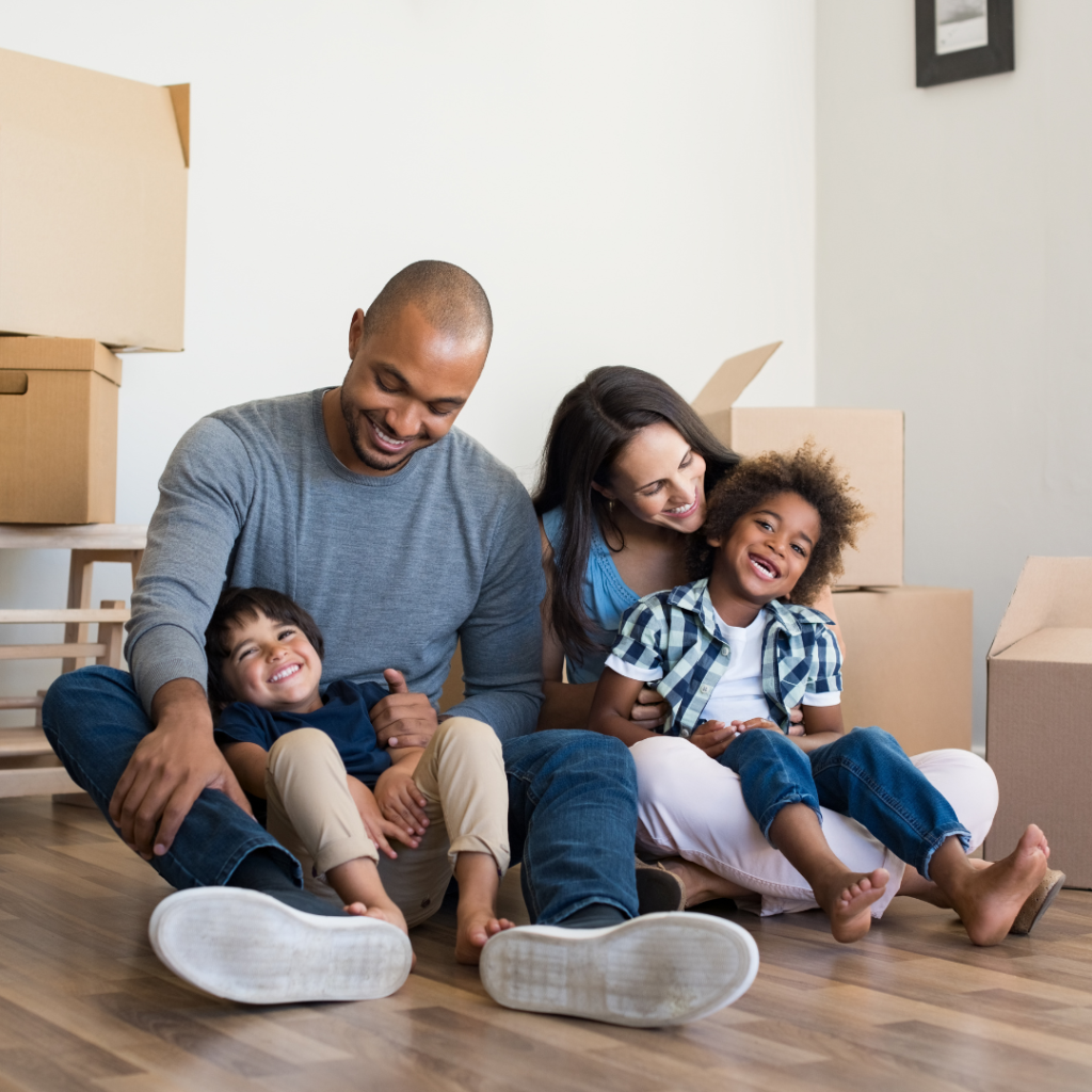Biracial family laughing sitting in a room with packing boxes around them.