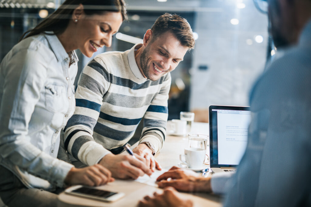 Young happy couple signing a document with their mortgage loan officer in an office. The view is through glass.