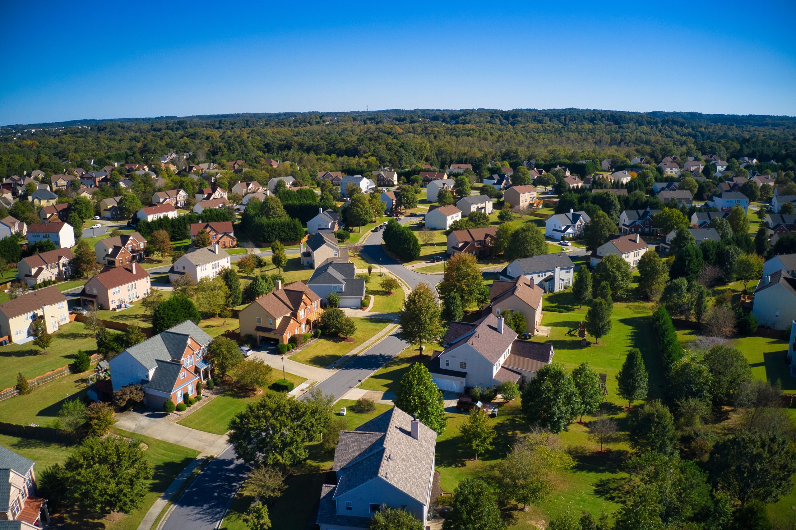 Shot using a drone during the golden hour shows an upscale suburbs with golf course, lake, houses and roof tops